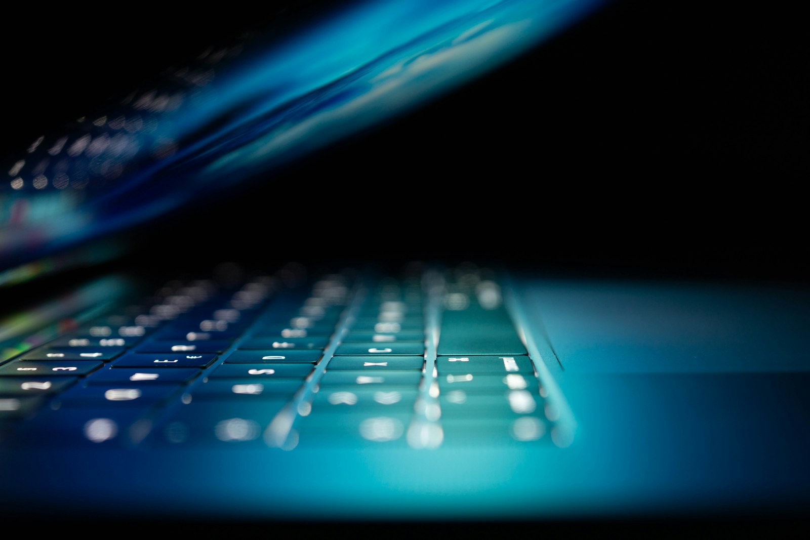 Laptop keyboard glowing in blue light in a dark room